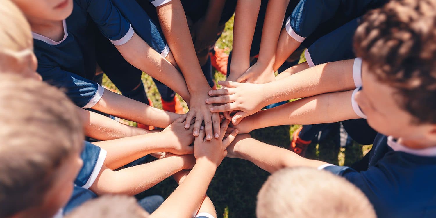 Young athletes in team uniforms stacking their hands together in a huddle.